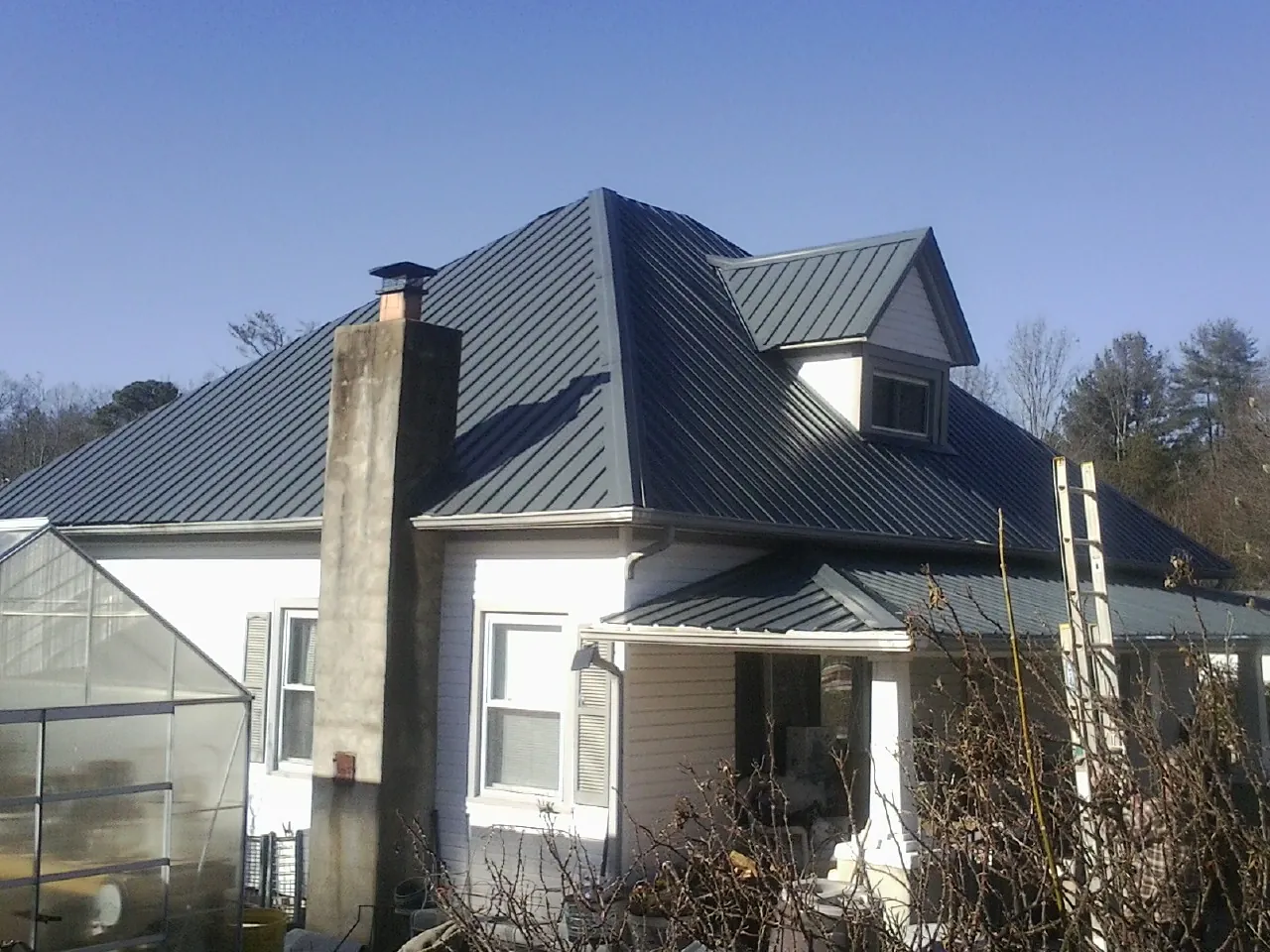 Dark blue standing seam metal roof on a white farmhouse with dormer — Slate & Tile Roof Repair by Roofing Brothers in Alexander