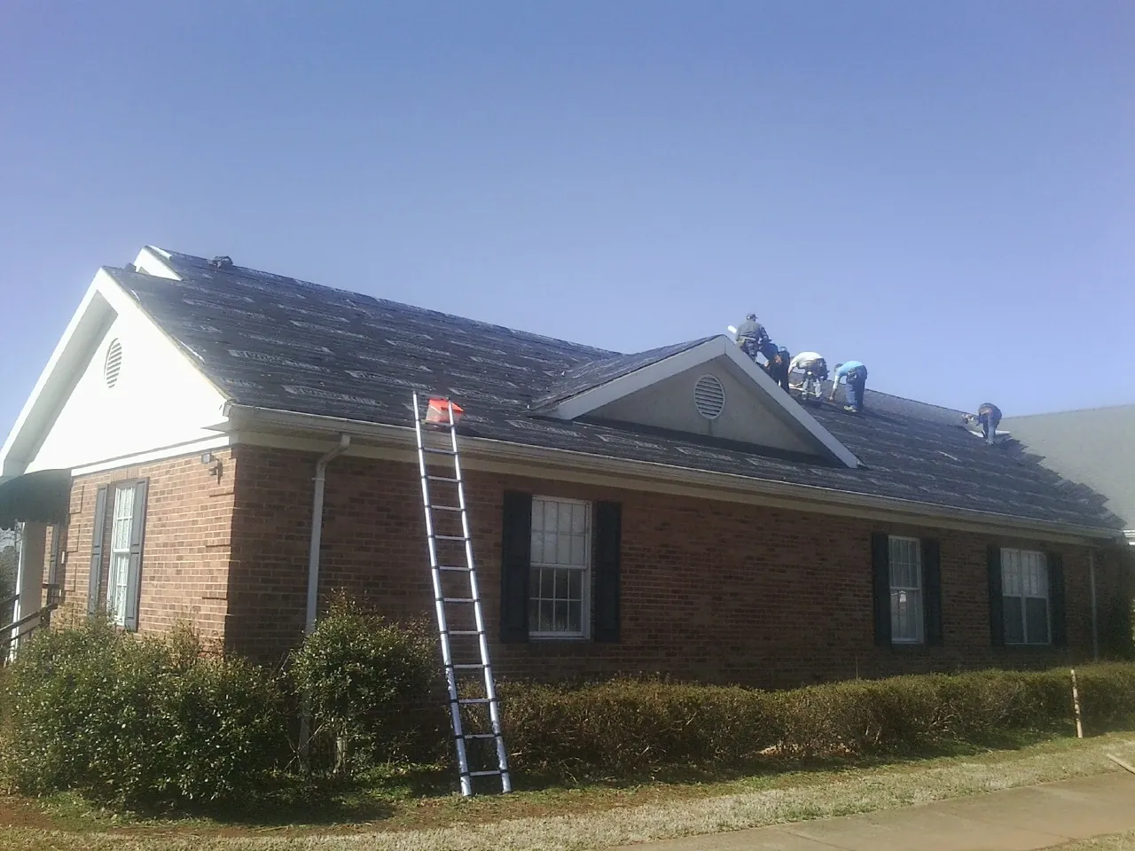 Crew tearing shingles off a brick ranch roof with a ladder set — Emergency Roof Repair work by our crew in Alexander