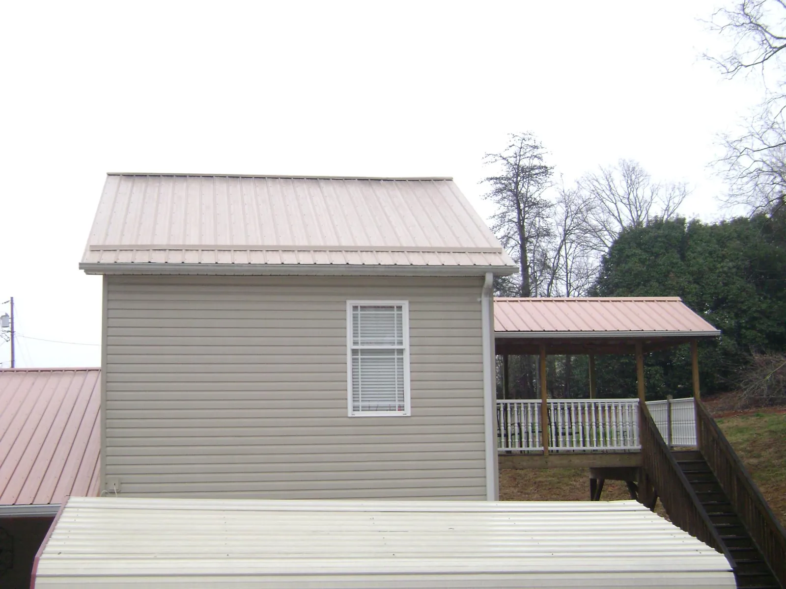 Tan metal roofs on a two story addition and attached porch, from a Roof Replacement job in Alexander